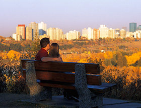 happy couple looking out across the Edmonton skyline from a park bench