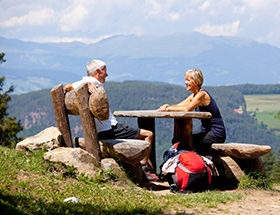 Older couple having a picnic at a table during a mountain hike