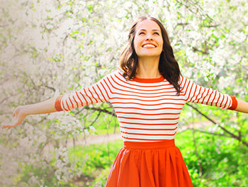 Woman standing in front of blossom trees, smiling into the sun